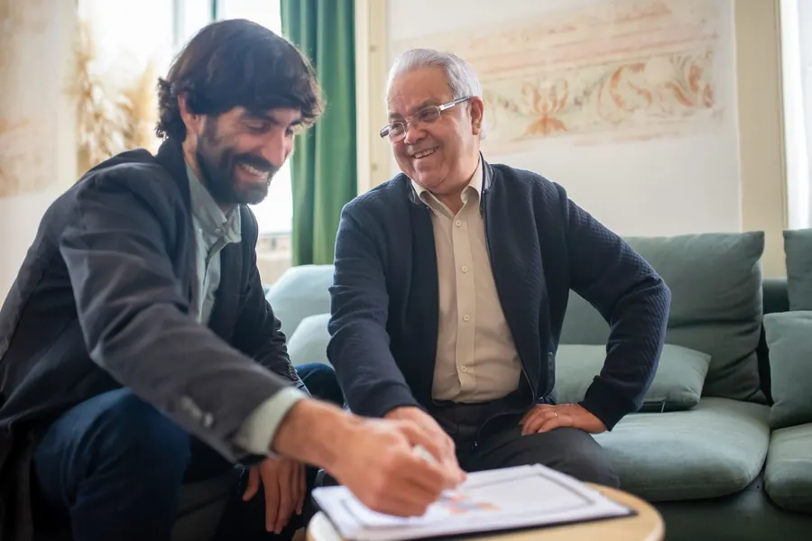 Contador sorrindo durante o atendimento a um cliente, com documentos sobre a mesa